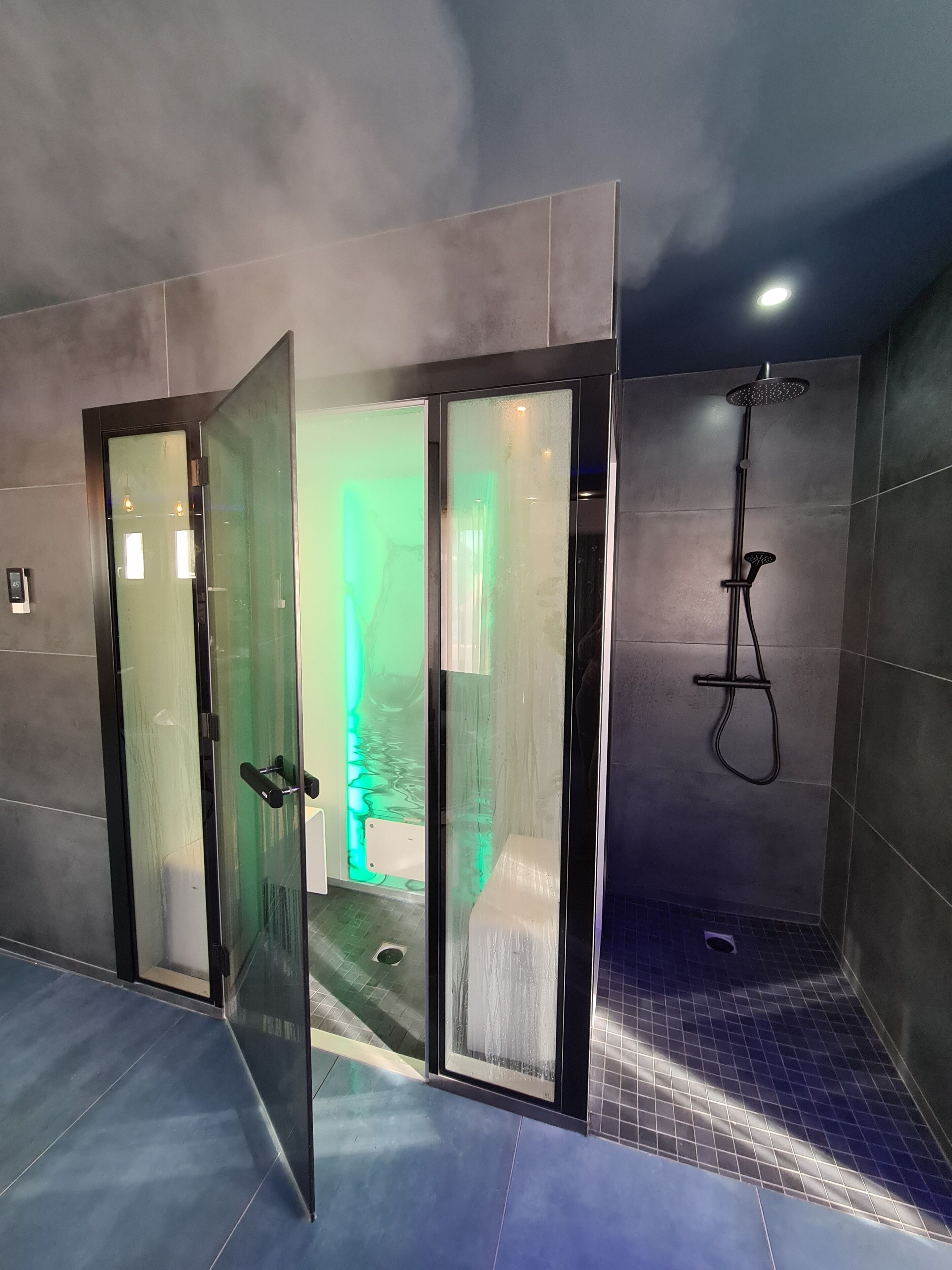 Un espace douche moderne doté d’une cabine de douche en verre, d’un pommeau de douche à main et d’un sol carrelé.