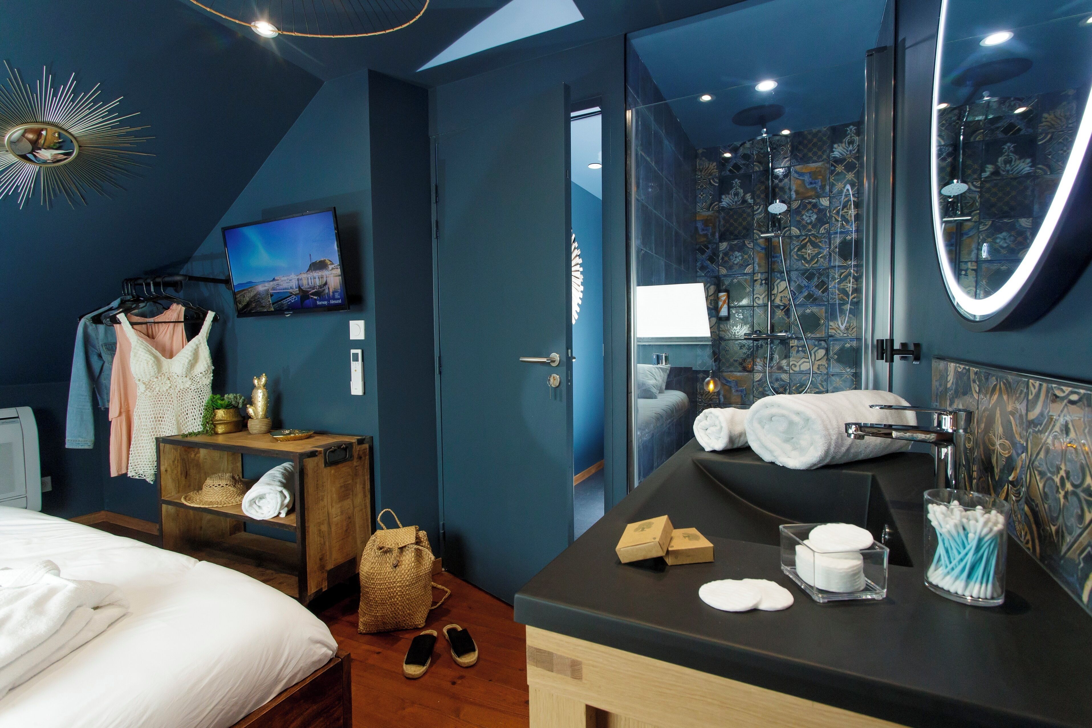 A modern hotel room with a large bed, a wooden nightstand, a vanity with a mirror, and a shower area with a glass door.