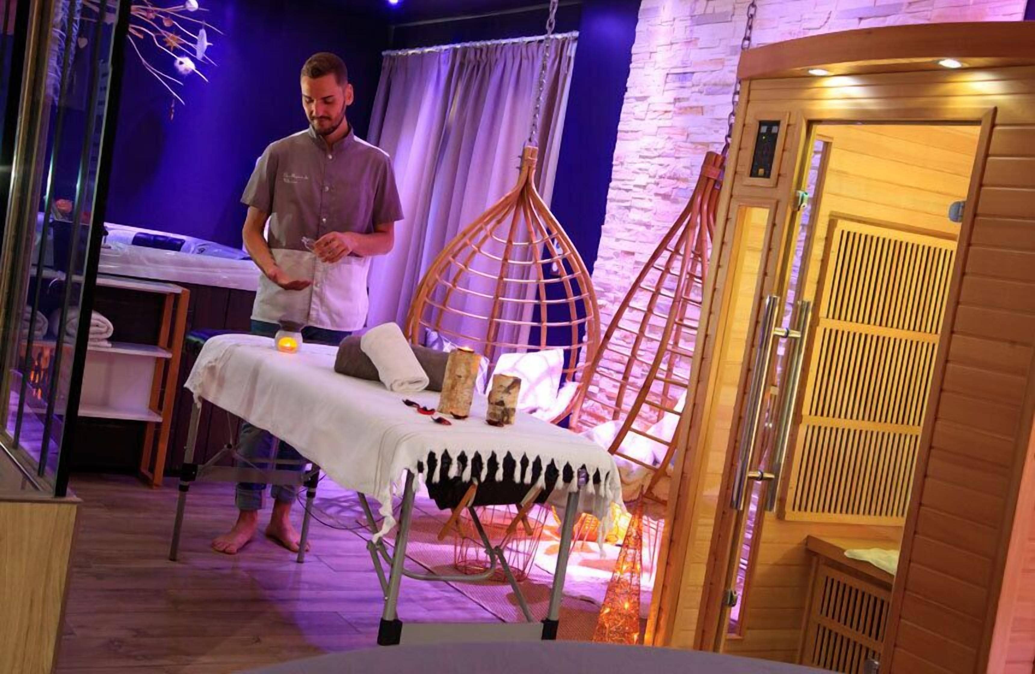 Ein Zimmer mit Massagetisch, einem Holzstuhl und einem kleinen Tisch mit Kerzen.