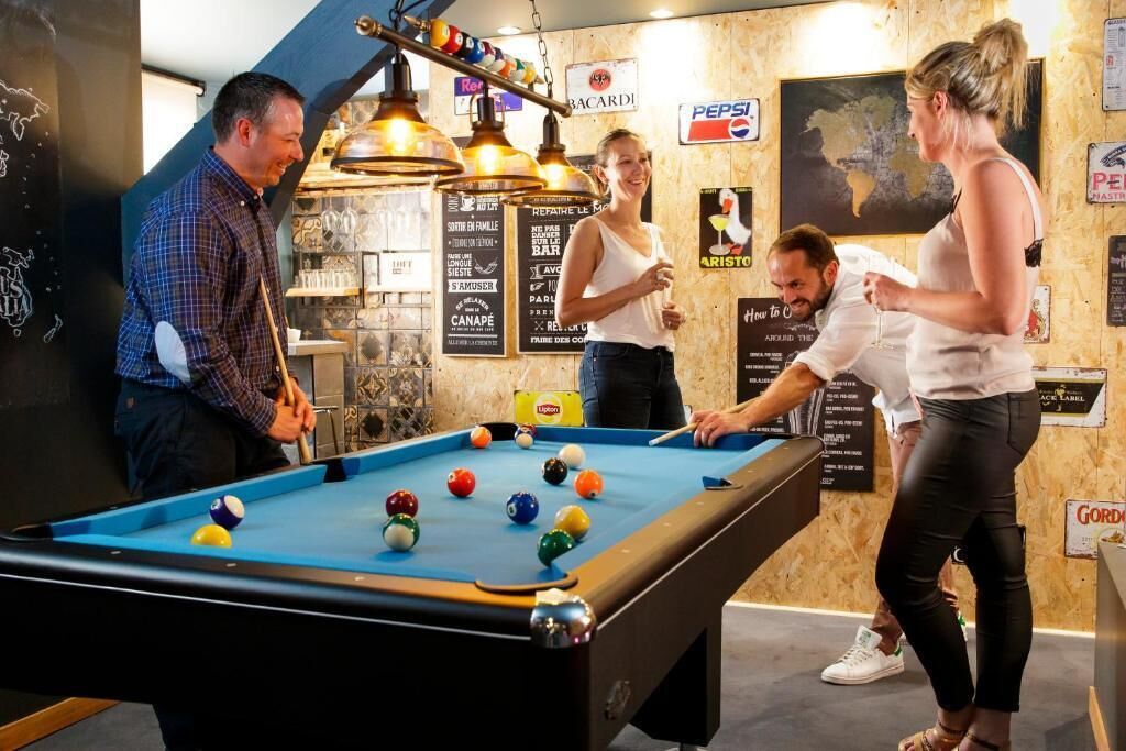 A pool table in a room with wooden walls, surrounded by people.