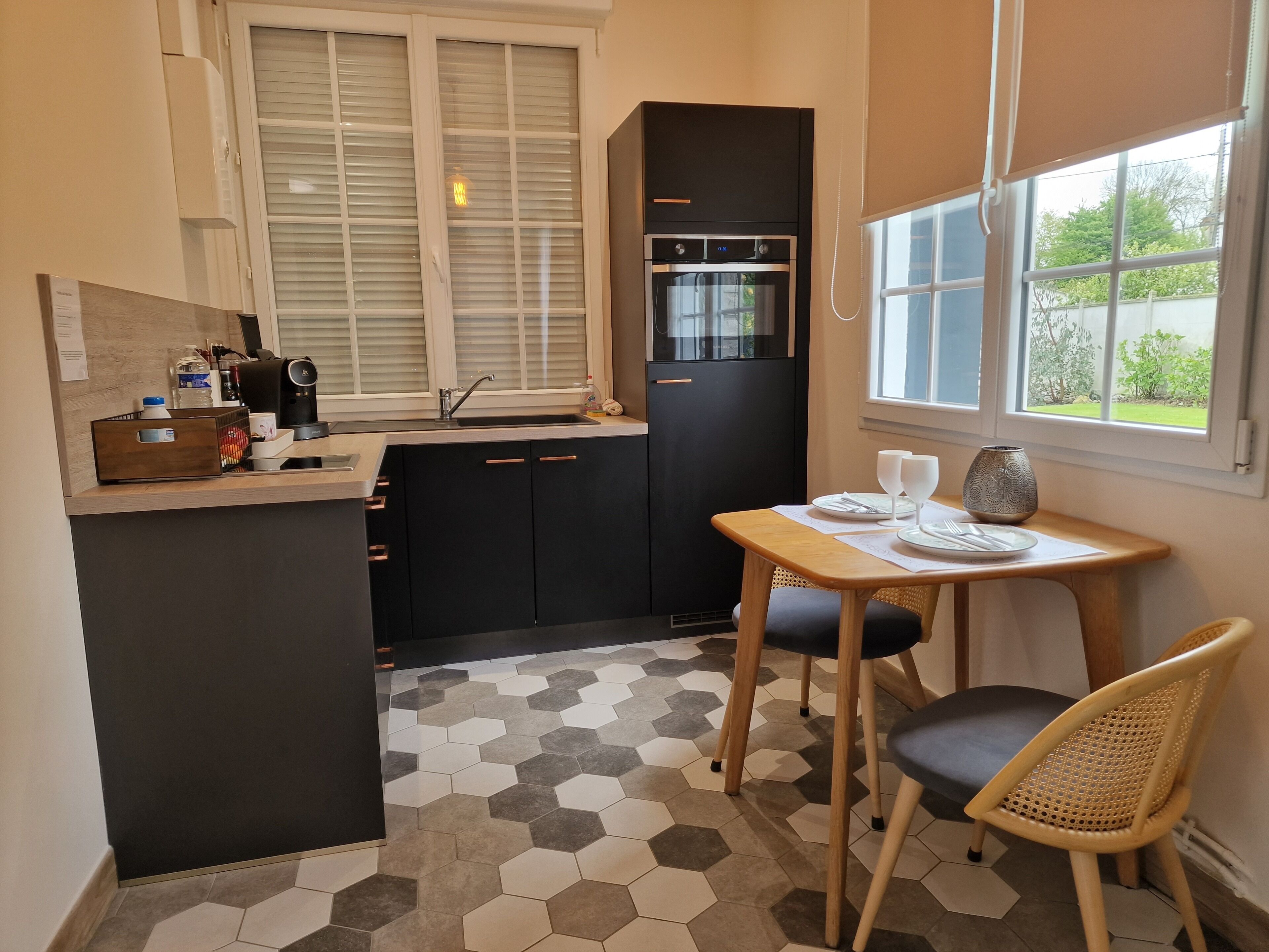 A compact kitchen with a black refrigerator, a built-in oven, a sink, and a window with blinds.