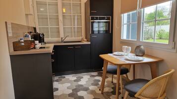 A compact kitchen with a black refrigerator, a built-in oven, a sink, and a window with blinds.