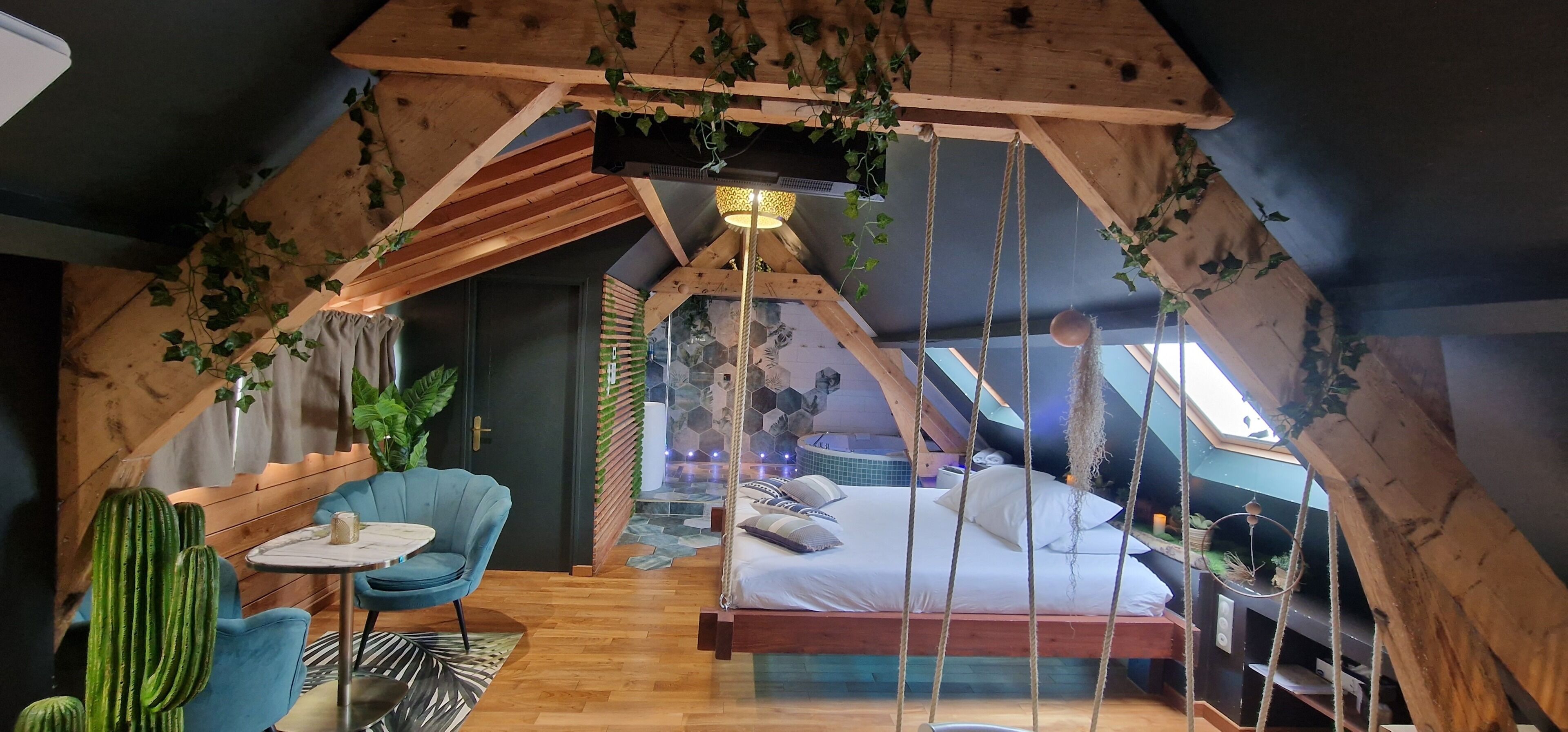 A cozy attic bedroom with a bed, a blue chair, a small table, and a hanging plant.