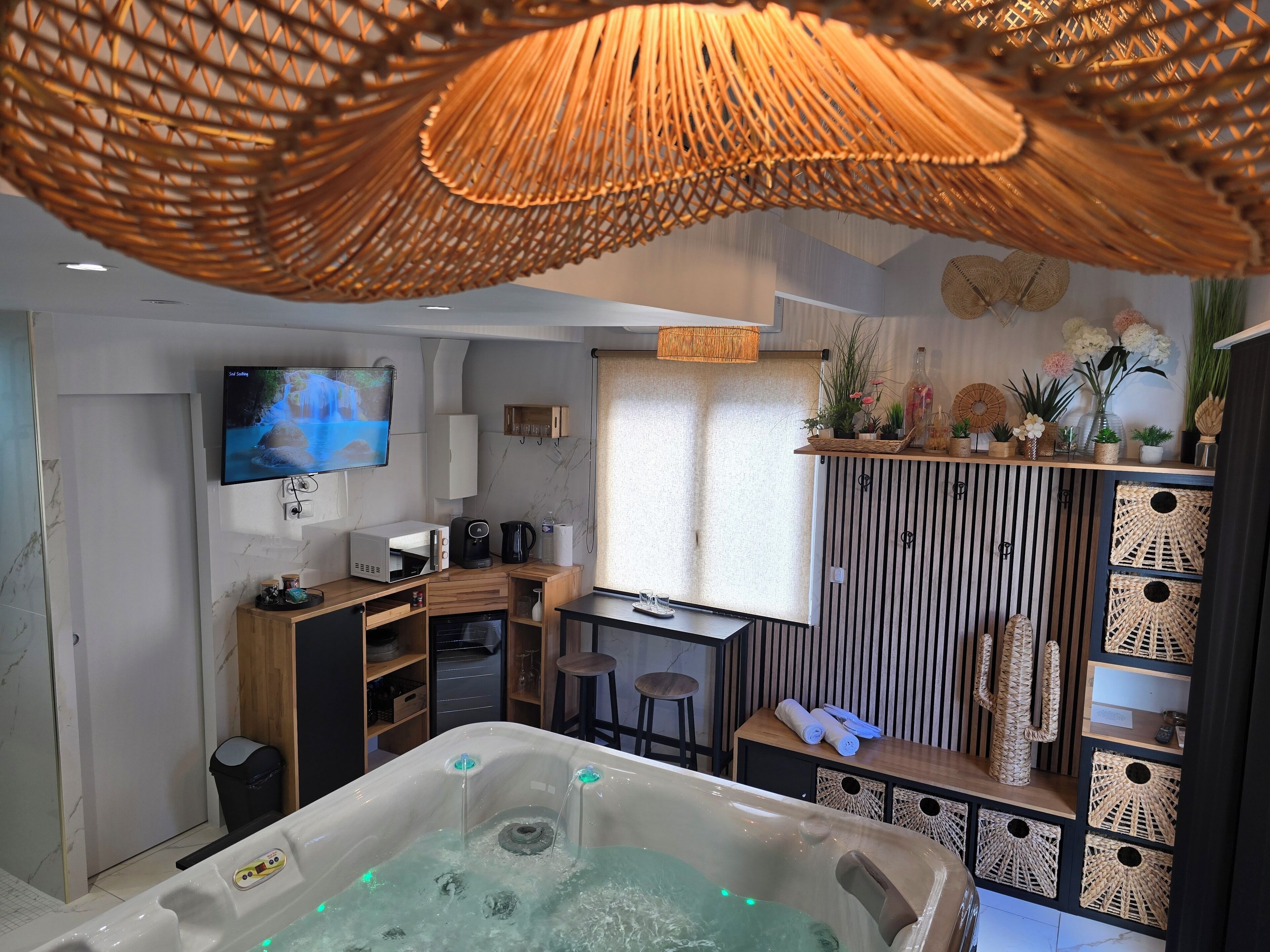 Et moderne badeværelse med et stort badekar, en bruseniche og et toilet. Der er en vaskebord med et spejl og en vask, og et fjernsyn ophængt på væggen.
