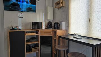 A compact kitchen with a built-in oven, a microwave, a coffee maker, and a TV displaying a waterfall scene.