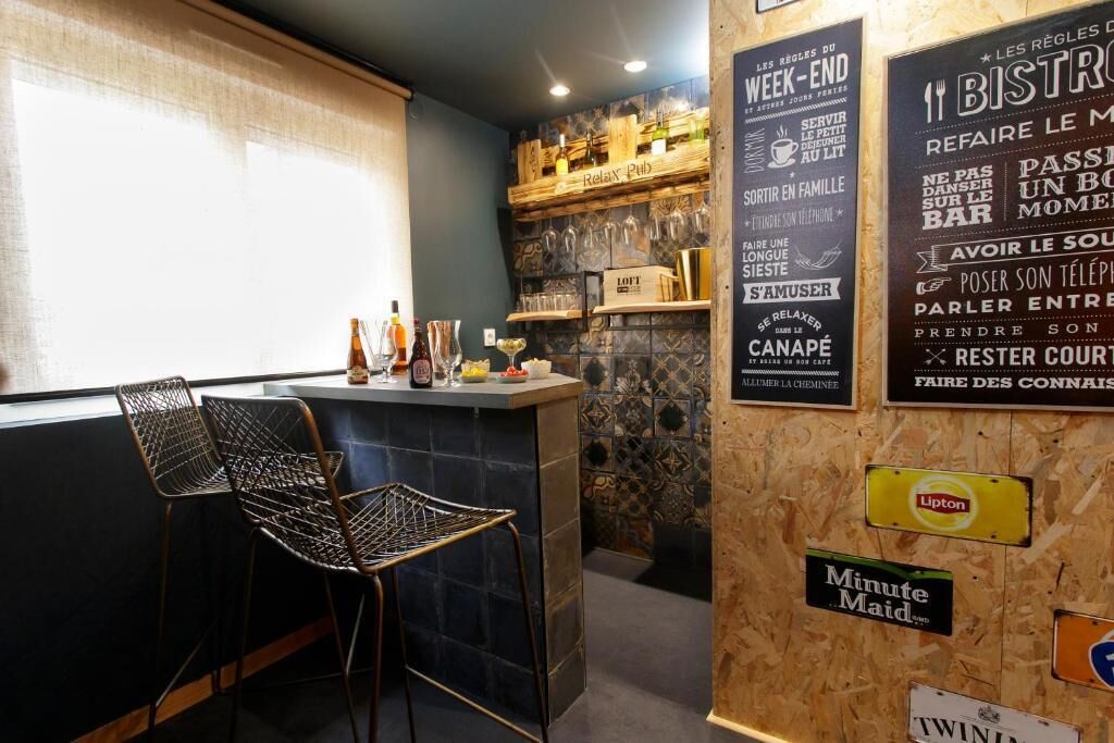 Un espace bar avec un comptoir, deux chaises en métal et un mur orné de divers panneaux et étiquettes.
