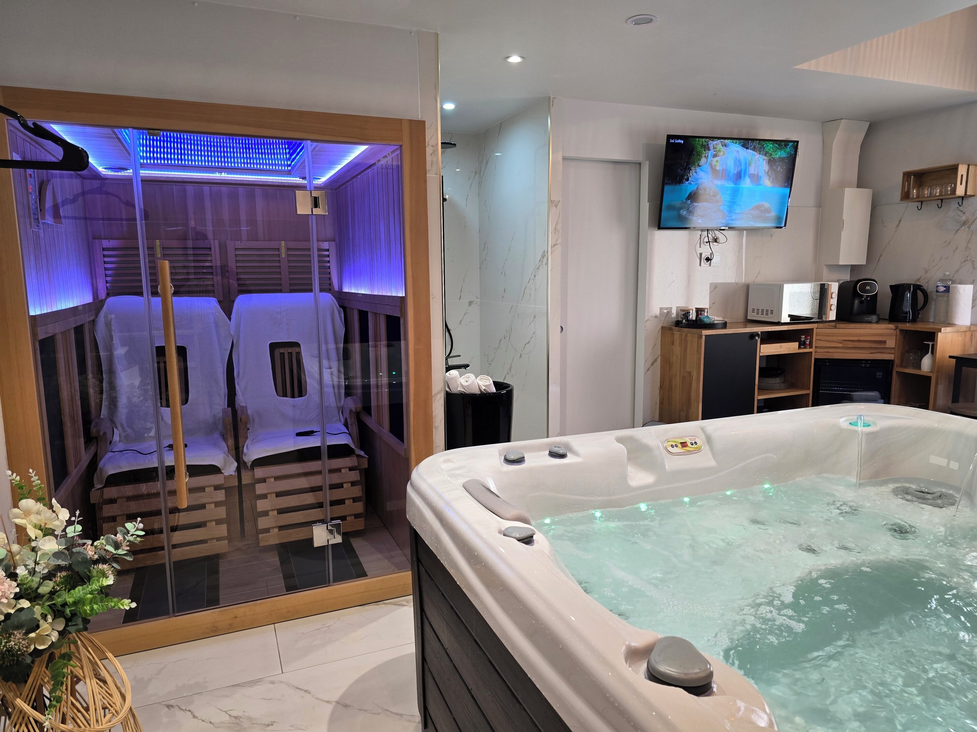 A modern bathroom with a jacuzzi, a shower enclosure with blue lighting, a television, and a wooden cabinet.