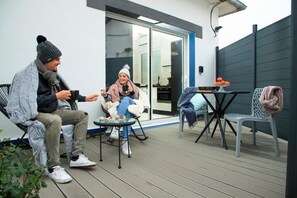 Two people seated on a deck with a table and chairs, a sliding glass door, and a dark fence. - Sweety Loft - Accommodation with Spa (Friville-Escarbotin)