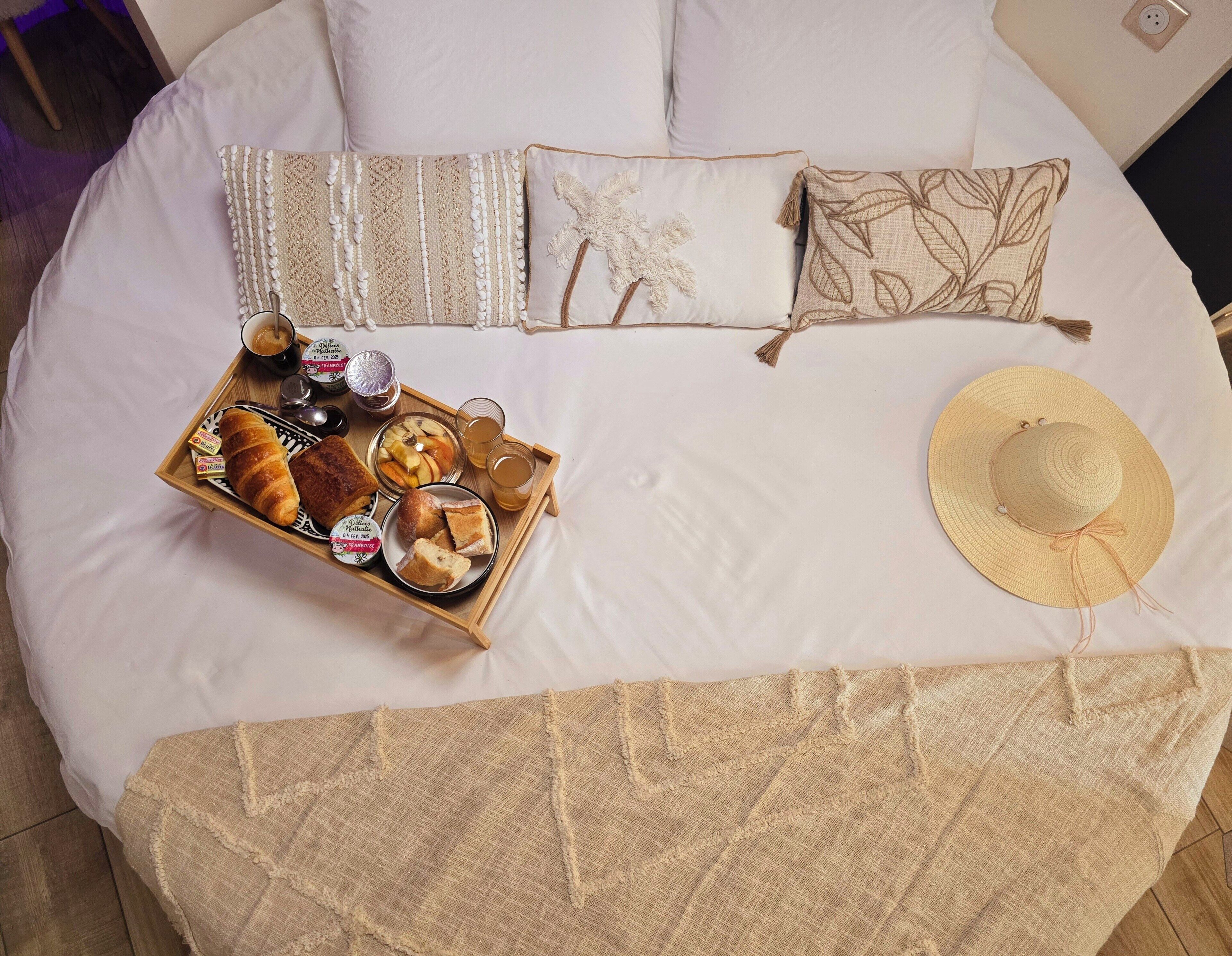 A neatly made bed with a tray of breakfast items, a straw hat, and decorative pillows.