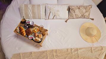 A neatly made bed with a tray of breakfast items, a straw hat, and decorative pillows.