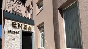 Un edificio con fachada de piedra, una puerta de entrada negra y el nombre 'ENZA SUITES' sobre la puerta.