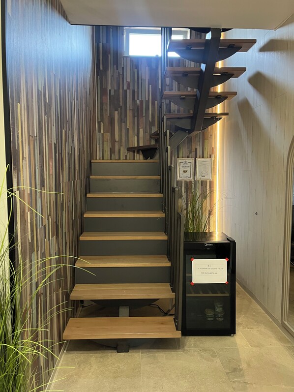 A staircase with wooden steps and a modern railing, leading to a landing with a framed certificate and a small plant.