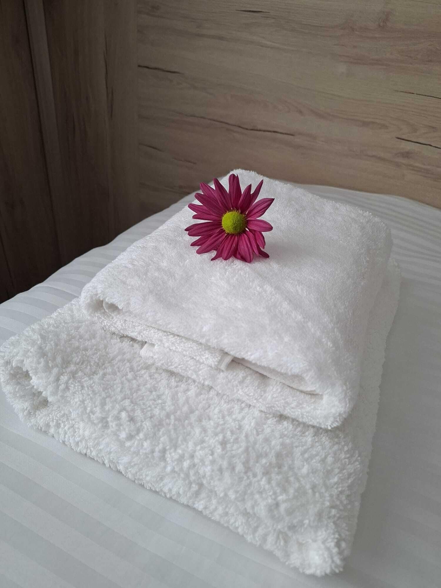 Una toalla blanca doblada con una flor rosa encima, sobre una superficie blanca.