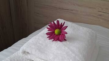 Una toalla blanca doblada con una flor rosa encima, sobre una superficie blanca.