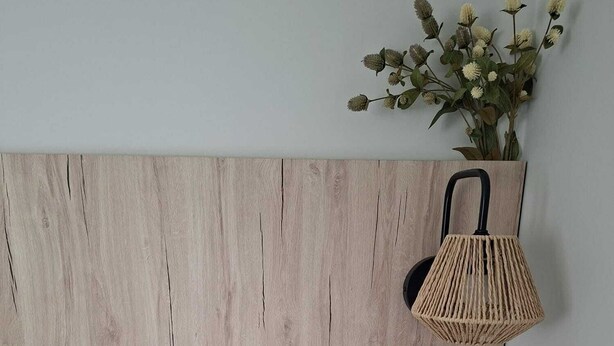 Un dormitorio con cabecera de madera, lámpara de noche, una pequeña planta en maceta y mesita de noche con cajón.