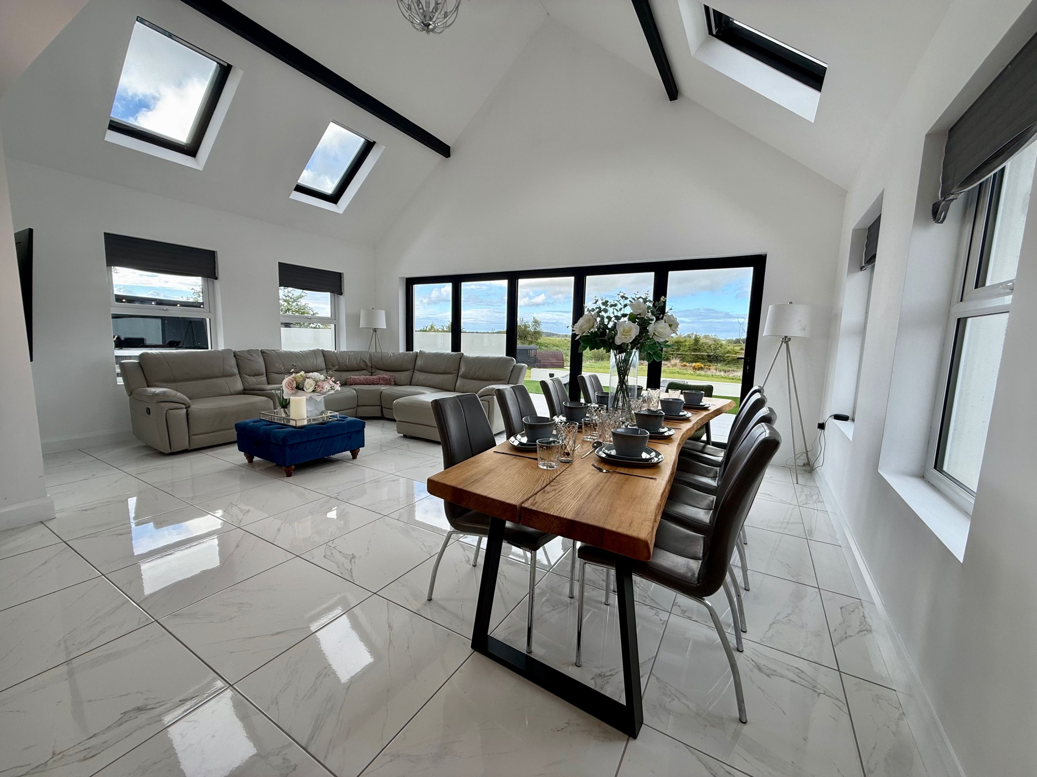 A spacious living area with a large dining table, a sofa, and a view of the outdoors.