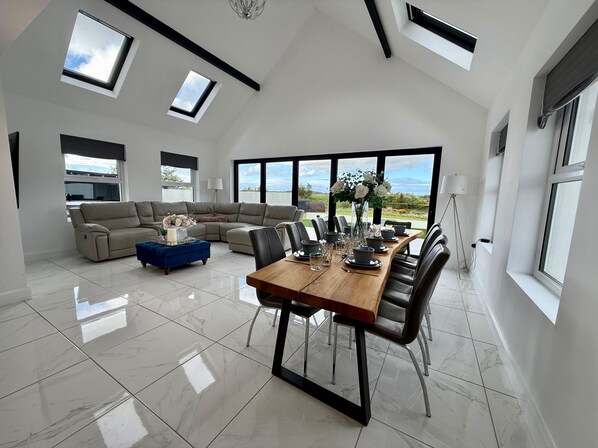 A spacious living area with a large dining table, a sofa, and a view of the outdoors.
