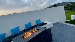 Une terrasse sur le toit dotée d’un foyer intégré, de sièges avec des coussins bleus et d’une vue sur la campagne.