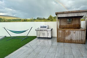 Une terrasse avec un barbecue, un coin bar en bois et un hamac.