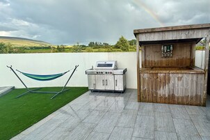 Un patio con una parrilla, una barra de madera y una hamaca.