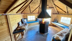 Une cabane chaleureuse avec un poêle à bois central, des bancs en bois et un plafond en pente.