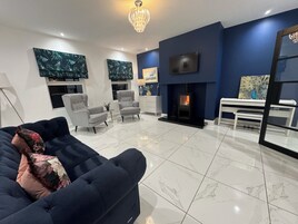 Una sala de estar moderna con chimenea, dos sillones, un sofá y un televisor montado en la pared.