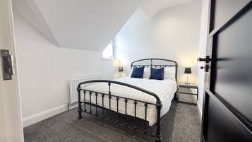 A bedroom with a bed, two bedside lamps, a radiator, and a window.
