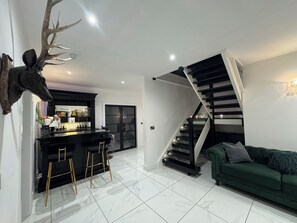 Un intérieur moderne avec un coin bar, un escalier et un canapé vert.