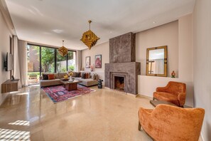 A spacious living room with a fireplace, a large window, and a modern chandelier. - Riad Jasmin – Al Maaden Golf – Marrakech (Marrakech)