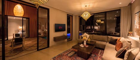 Uma sala de estar moderna com um sofá grande, uma mesa de centro, uma televisão e um lustre.