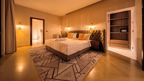 A modern hotel room with a large bed, a patterned rug, built-in shelving, and a door leading to another room. - Riad Jasmin – Al Maaden Golf – Marrakech (Marrakech)