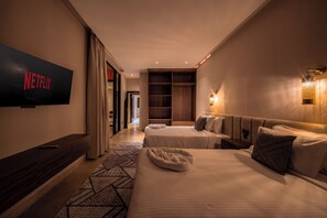 Een hotelkamer met een grote flatscreen televisie, twee bedden, een houten garderobe, een kamerkleed met dessin en een wandlamp.