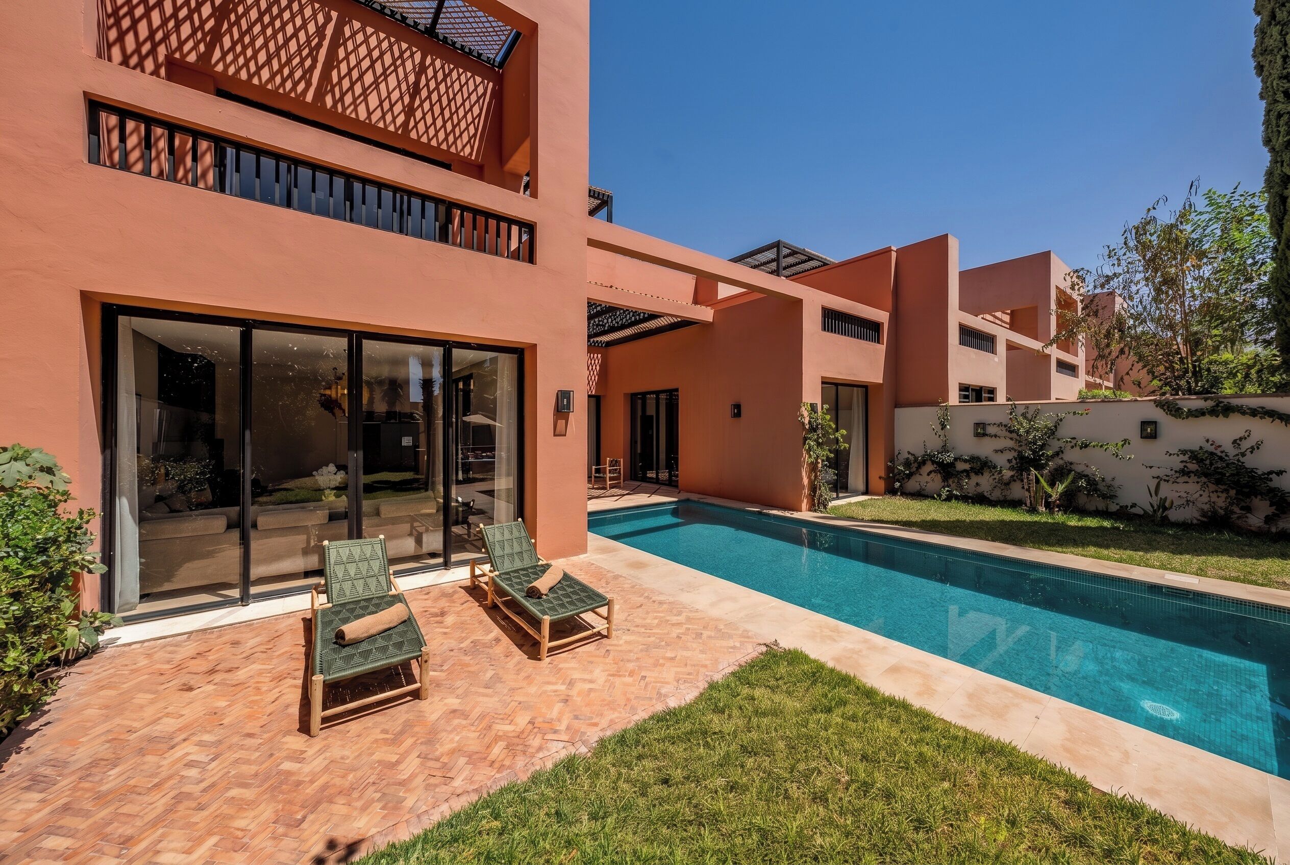 A modern two-story building with a swimming pool, outdoor seating, and a well-maintained lawn.