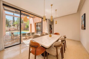 A dining area with a large table, chairs, and hanging pendant lights. - Riad Jasmin – Al Maaden Golf – Marrakech (Marrakech)
