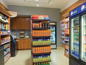 Interior de um supermercado com um refrigerador de bebidas, prateleiras repletas de diversas bebidas e um espaço para café.