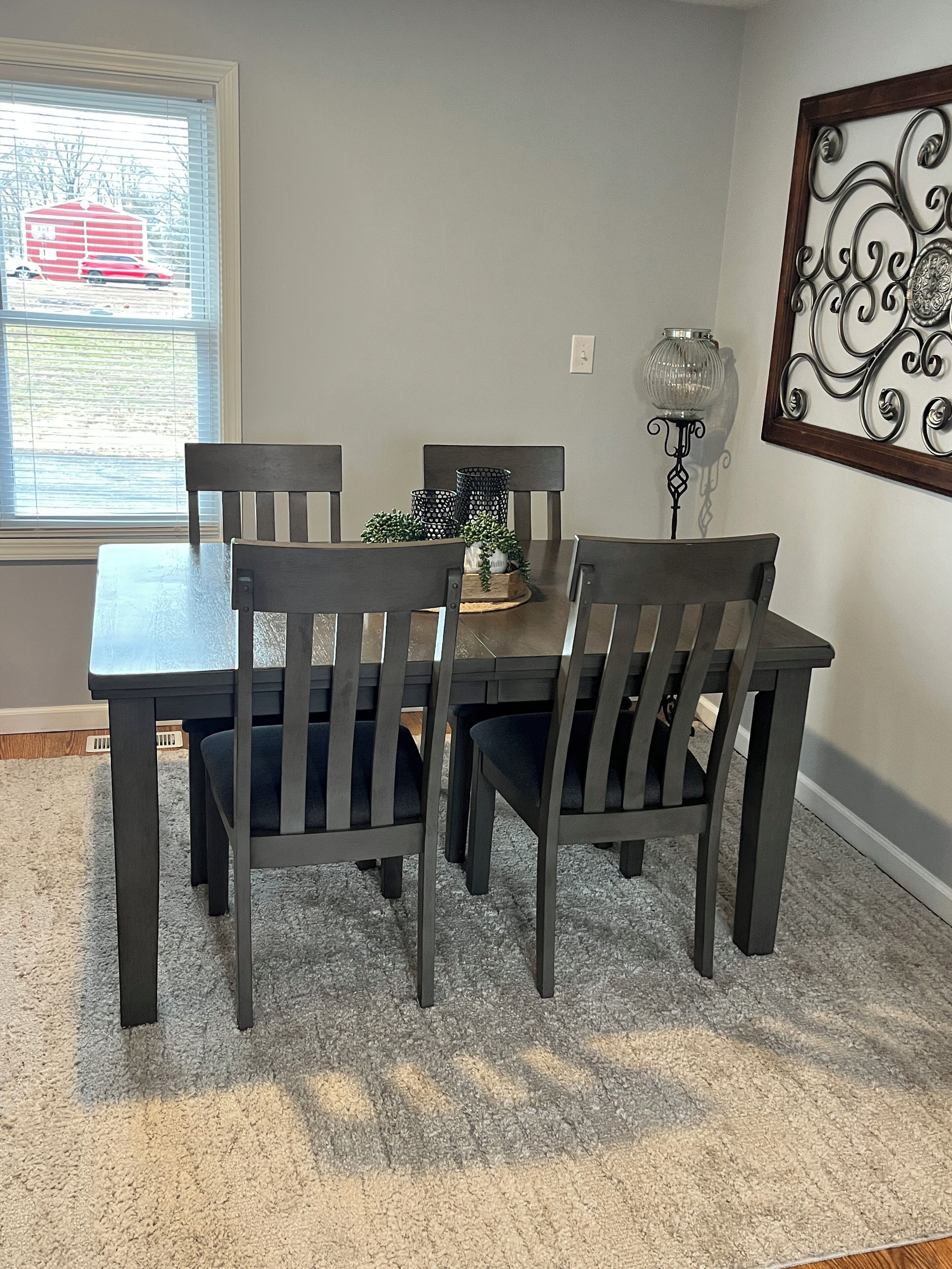 Un coin repas avec une table et des chaises, un élément décoratif mural et une fenêtre avec des stores.