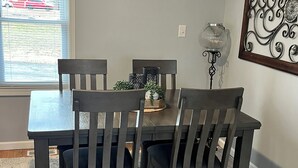 Un comedor con una mesa y sillas, un adorno en la pared y una ventana con persianas.