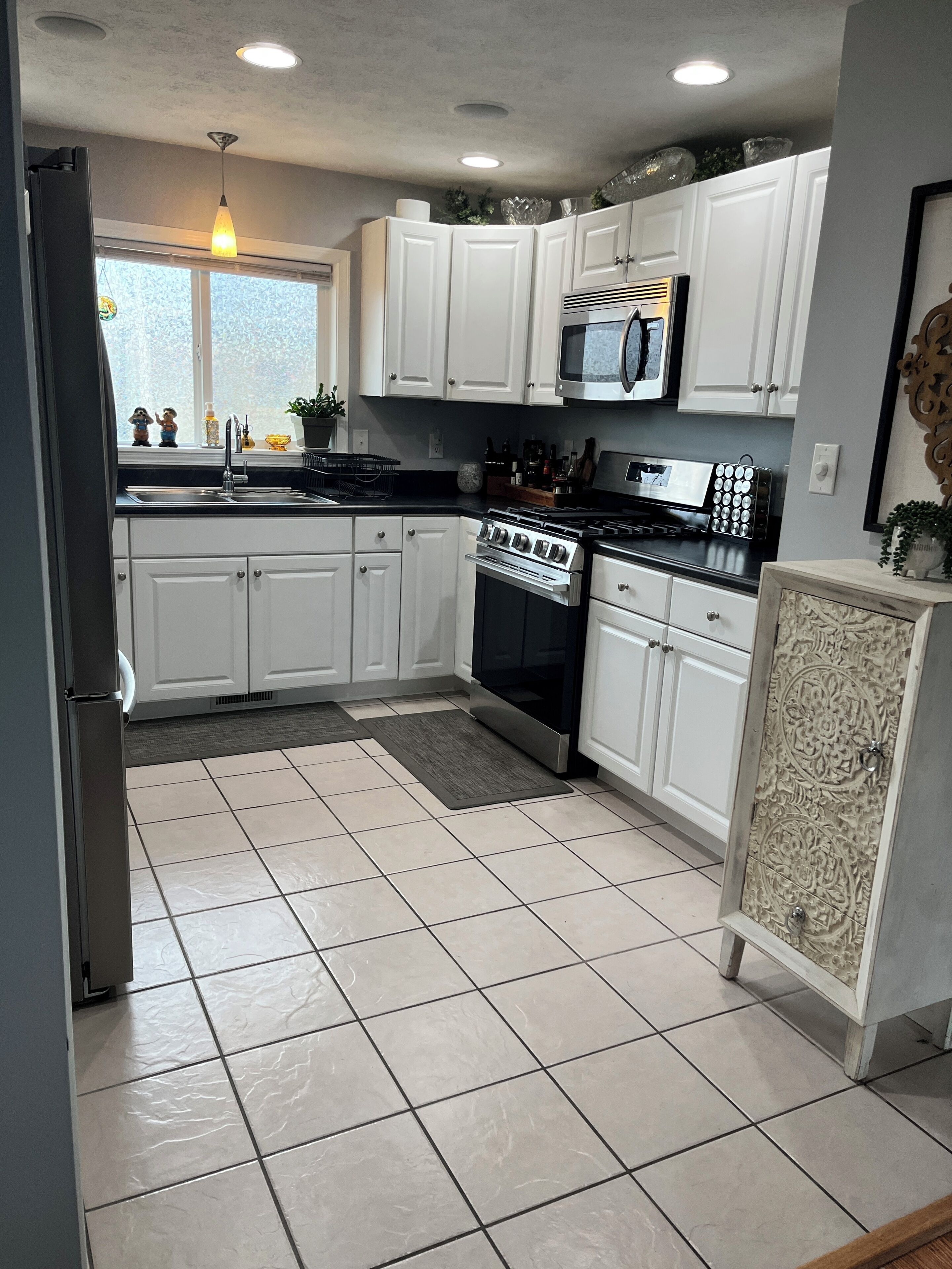 Una cocina con alacenas blancas, estufa de acero inoxidable, microondas y refrigerador.