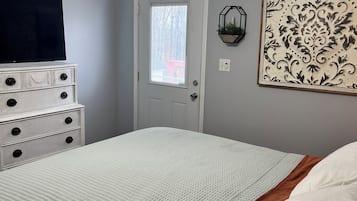 Una camera da letto con un letto, una cassettiera, una ventola a soffitto, una TV a muro e una porta con finestra.