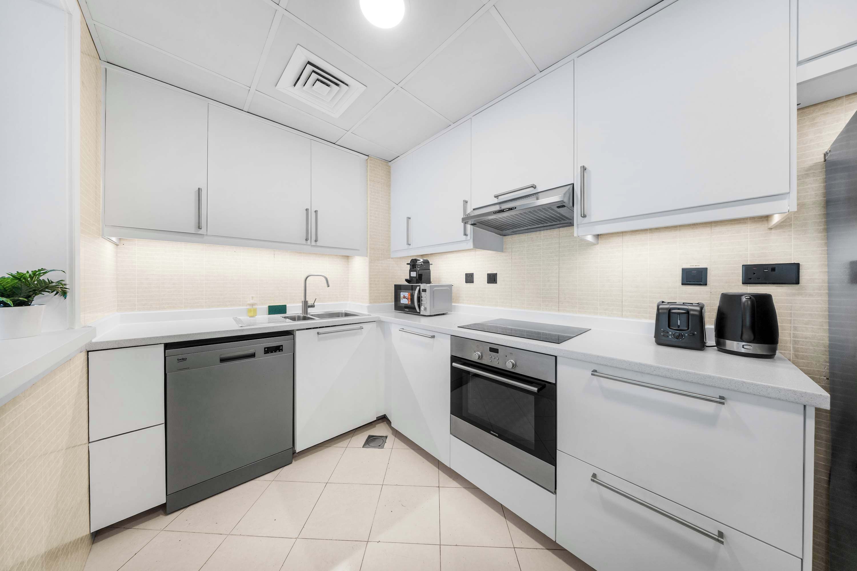 A modern kitchen with white cabinets, a dishwasher, an oven, a coffee maker, and a toaster.