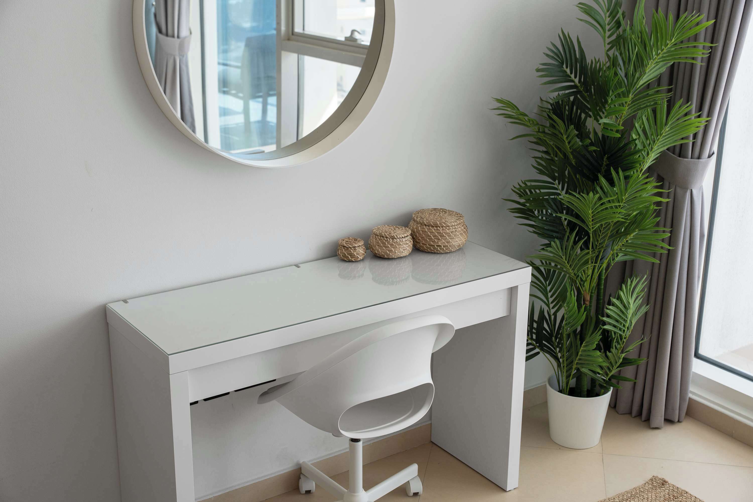 Un escritorio blanco con un espejo, una planta en maceta y un taburete pequeño.