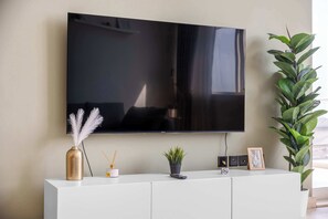Ein Flachbildfernseher ist an einer Wand über einer weißen Konsole angebracht, auf der sich eine Vase, eine kleine Pflanze und ein Bilderrahmen befinden.