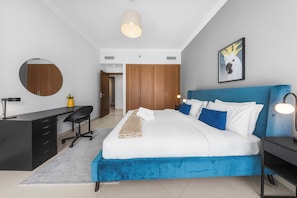Ein modernes Schlafzimmer mit einem großen Bett, einem Schreibtisch, einem Stuhl, einem Kleiderschrank und einem gerahmten Bild an der Wand.