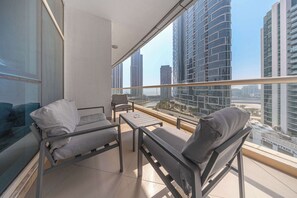 Ein Balkon mit zwei Stühlen und einem kleinen Tisch, der auf einen Stadtblick mit hohen Gebäuden blickt.