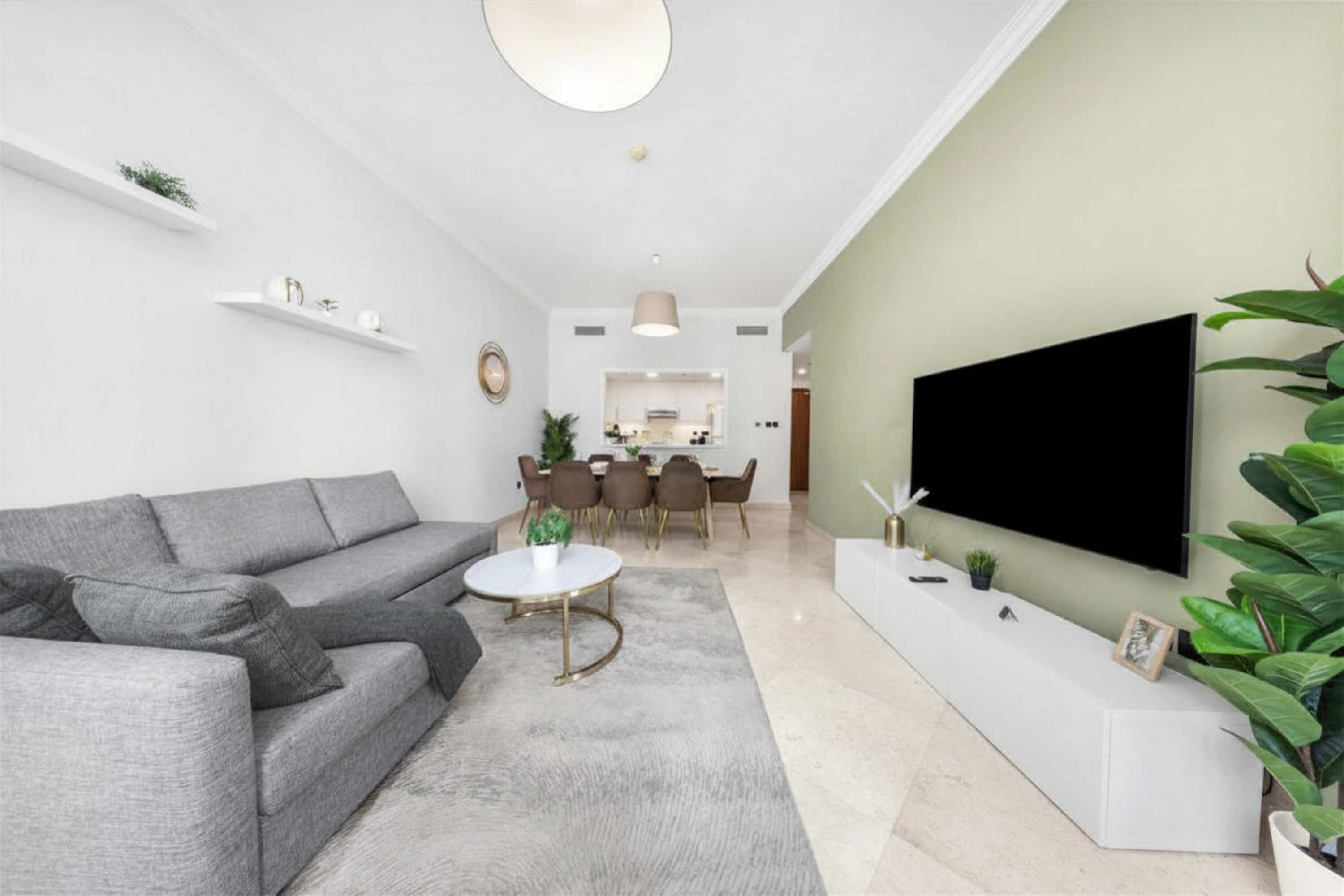 A modern living room with a grey sofa, a round coffee table, and a flat-screen TV mounted on the wall.
