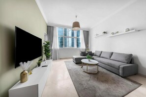 Ein modernes Wohnzimmer mit Flachbildfernseher, grauem Sofa, rundem Couchtisch und einem großen Fenster mit Vorhängen.