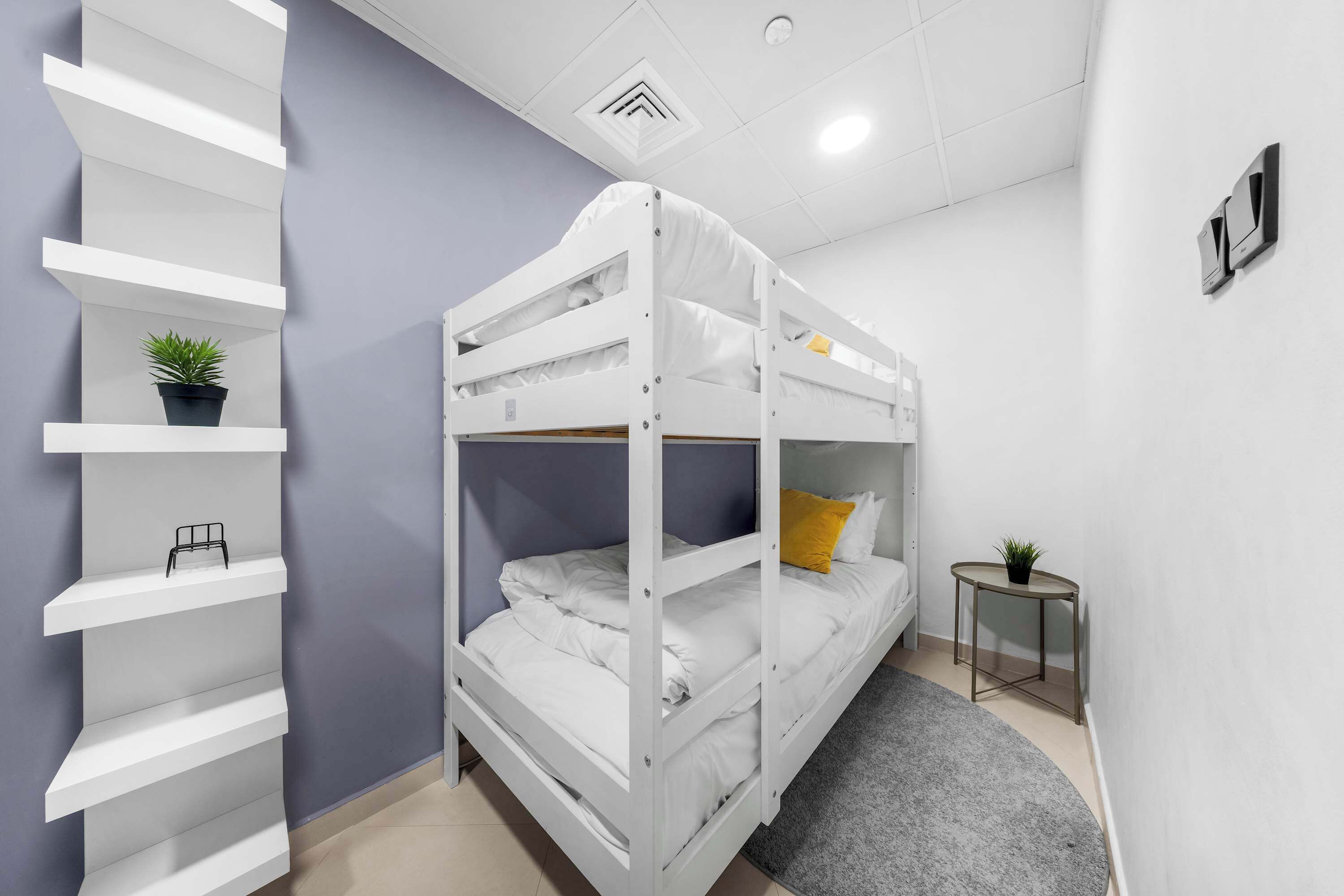 Ein Stockbett mit einer Regaleinheit und einem kleinen Tisch mit einer Pflanze.