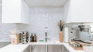 A modern kitchen with white cabinets, a stainless steel sink, a coffee machine, and a vase with dried plants.