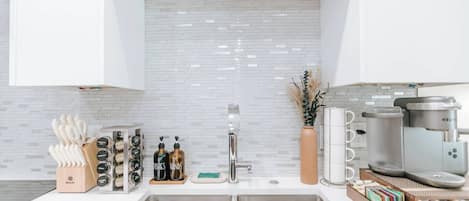 A modern kitchen with white cabinets, a stainless steel sink, a coffee machine, and a vase with dried plants.