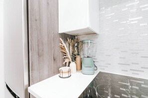 Uma cozinha com bancada branca, liquidificador e plantas decorativas.